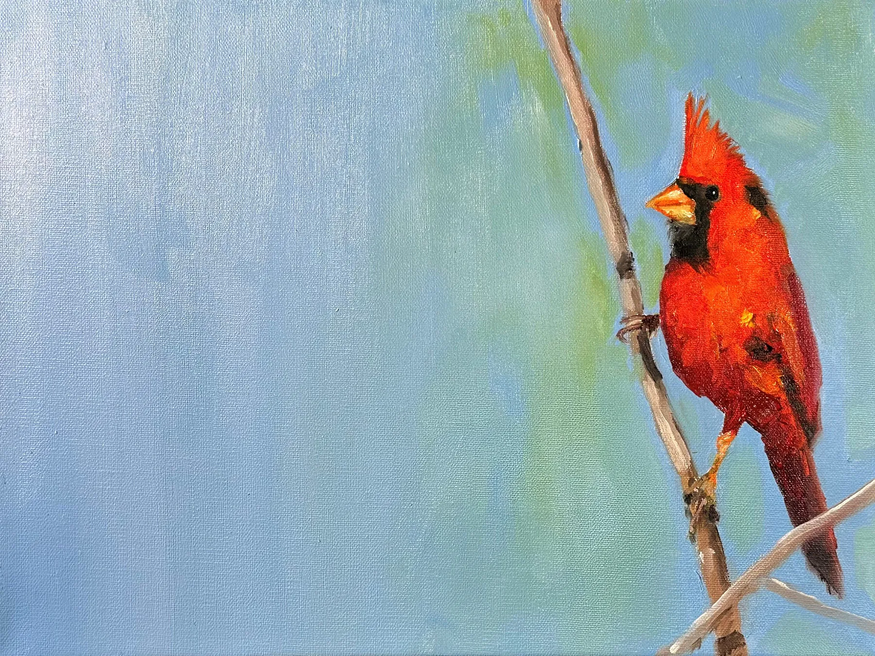 A cardinal positioned on the right side of a warn blue field, a shimmer of green leaves, with open space extending to the right.